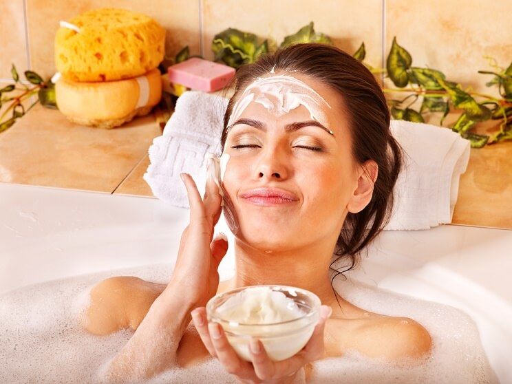 woman exfoliating face in bathrub