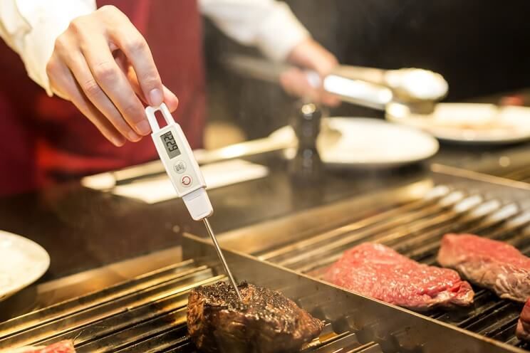 man checking steak on grill with meat thermometer