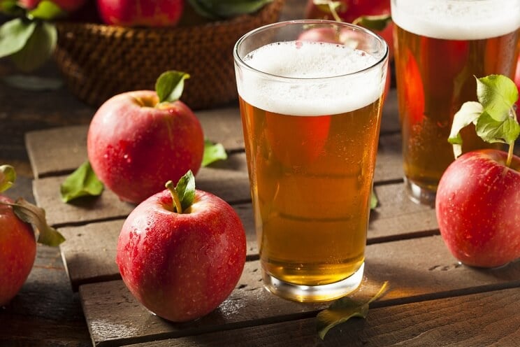 hard apple cider in a beer glass with apples on a hardwood surface