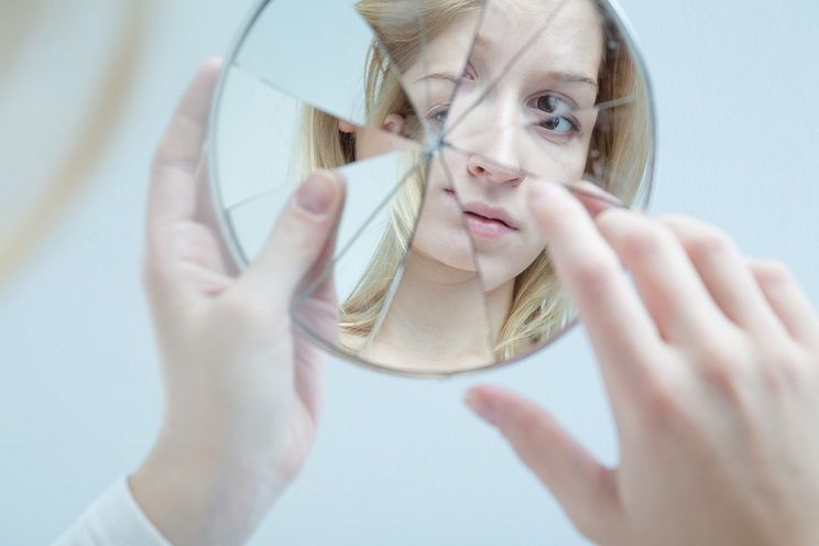 insecure girl looking into a broken mirror