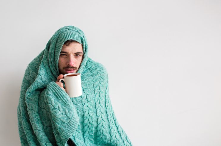 man drinking teas wrapped in a knitted blanket
