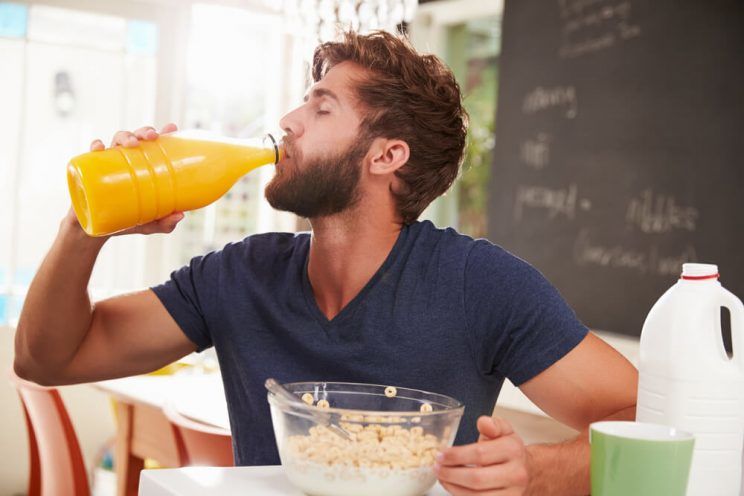 Young Man Eating Breakfast And Drinking Orange Juice