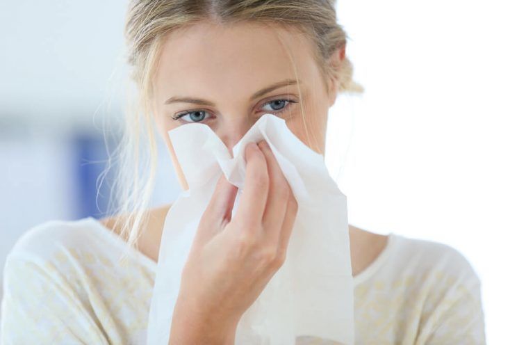 Young woman with cold blowing her runny nose