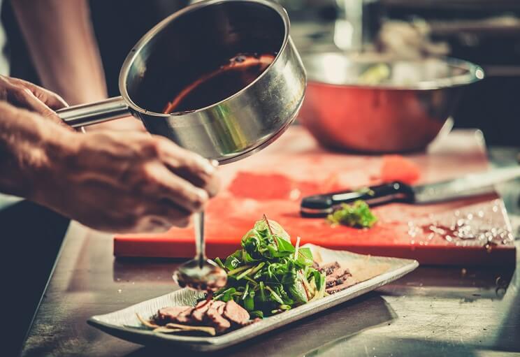 chef pouring sauce over greens and meat