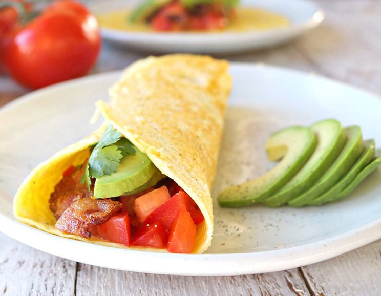 Le bacon, la tomate et l'avocat sont enroulés dans une galette d'œufs riche en protéines pour un burrito à déjeuner sans gluten.