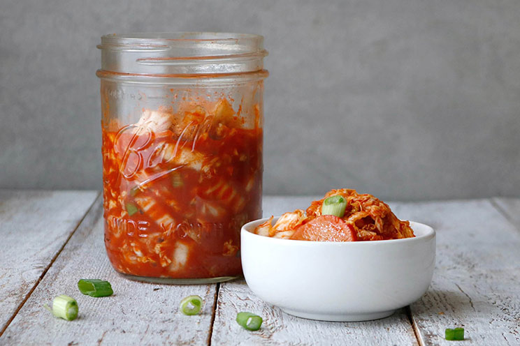 Shredded cabbage ferments with radishes, scallions, and ginger for a homemade, Paleo-friendly kimchi rich in gut-healing probiotics.