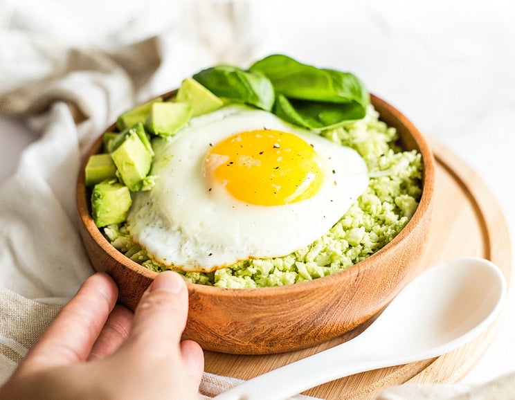Wake up to this delicious keto low-carb breakfast bowl - a tasty pesto cauliflower rice topped with a fried egg, diced avocados, and fresh spinach.